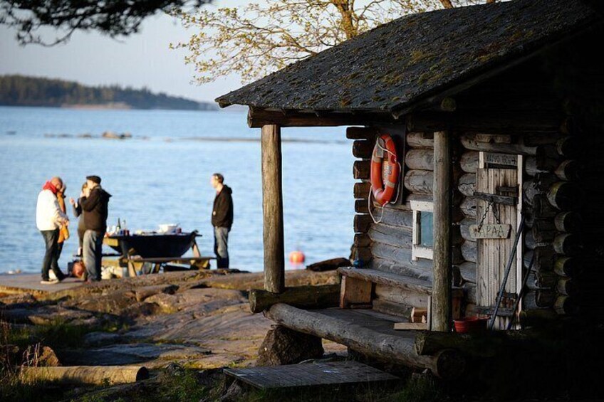A wooden cabin by a lake with people gathered around a cart. 5