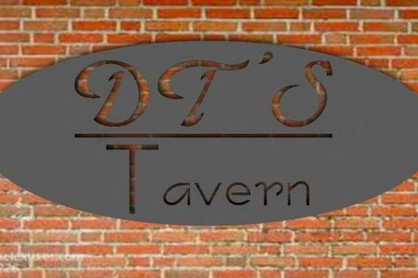 A metal sign with 'DT's Tavern' written on it, mounted on a brick wall. 4