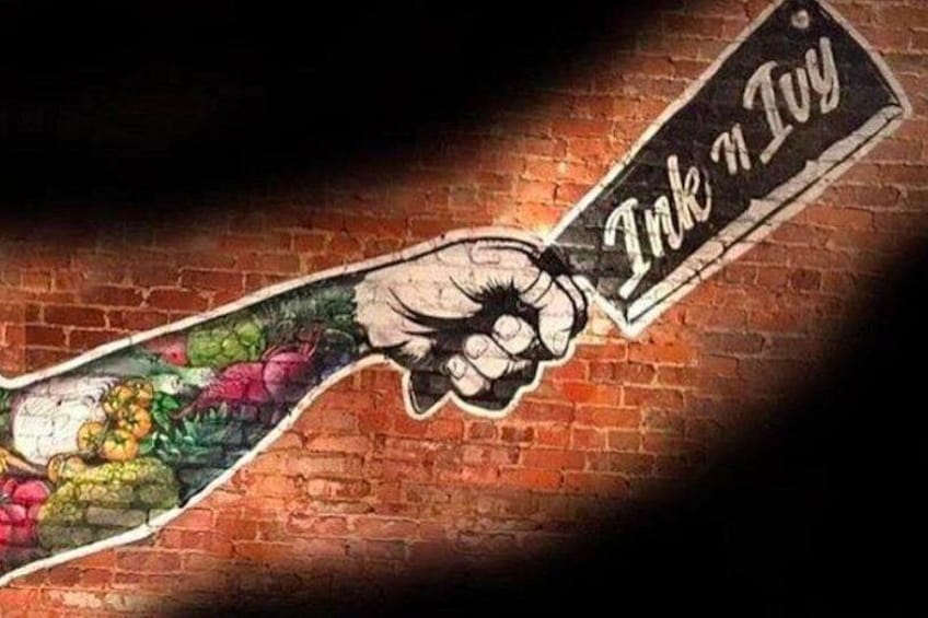 A graffiti of a clenched fist with the words 'Ink n Ivy' on a brick wall. 5