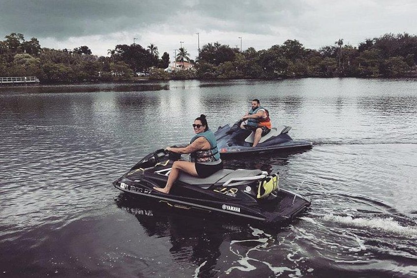Dos personas en un jet ski sobre un lago tranquilo, con árboles y un cielo nublado al fondo. 2