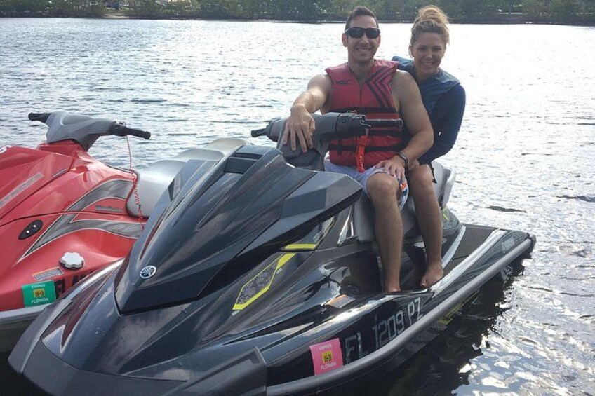 Dos personas en un jet ski, con otros dos jet skis, uno rojo y otro negro, al fondo. 3
