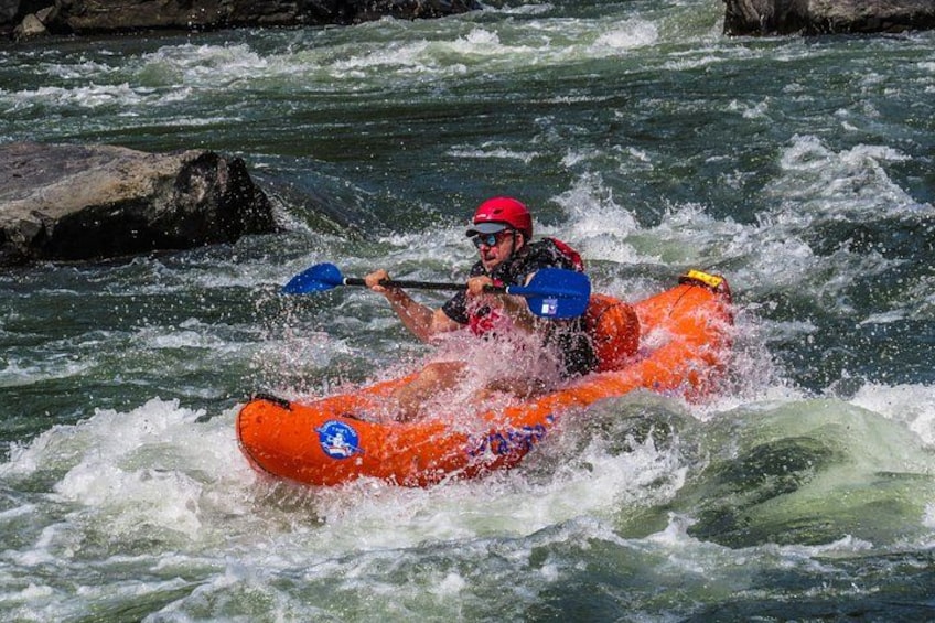 Una persona con casco rojo y kayak naranja remando en un río de aguas blancas. 4