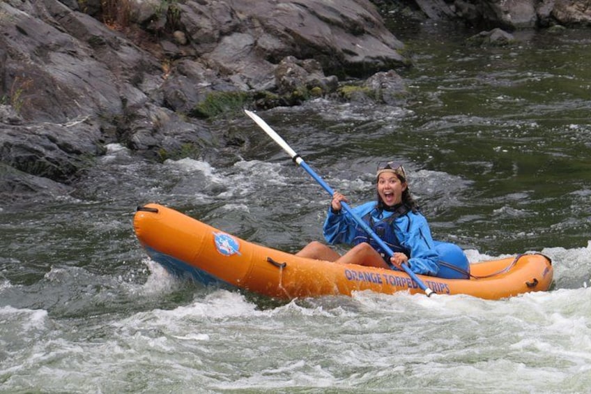 Una persona con una chaqueta azul remando un bote naranja con la leyenda 'Orange Torpedo Trips' en un río. 3