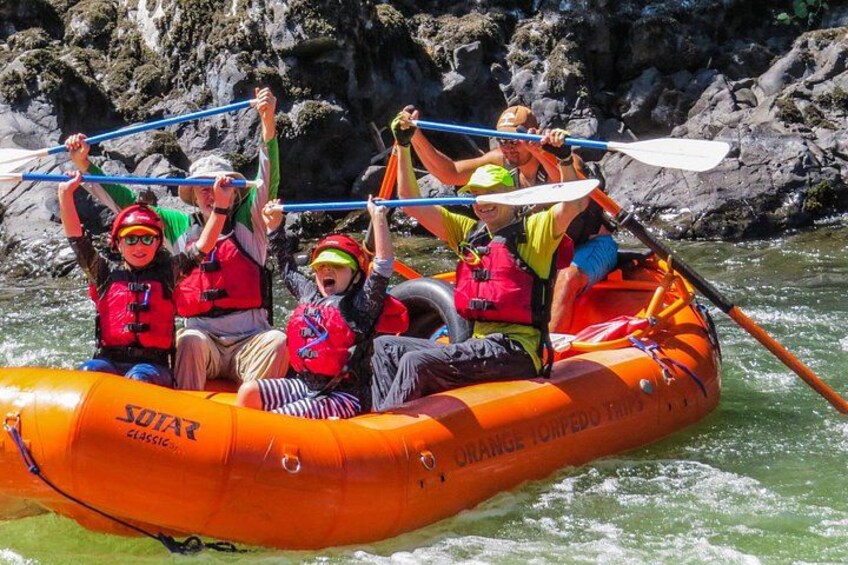 Un grupo de personas en una balsa naranja en un río, usando chalecos salvavidas y remos. 1