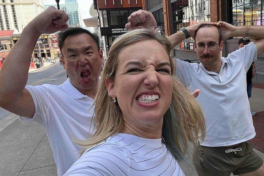 Drei Personen machen ein Selfie auf einer Stadtstraße, im Hintergrund sind Gebäude zu sehen. 2