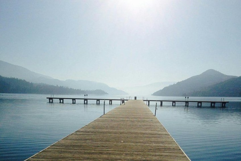 Eine Holzstege führt ins ruhige Wasser, im Hintergrund erheben sich Berge. 5