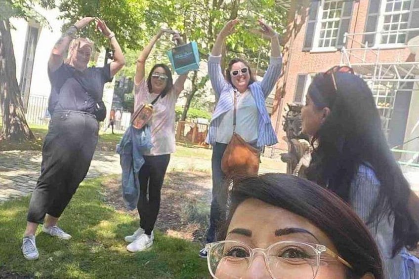 Eine Gruppe von Menschen draußen, einige halten Gegenstände hoch, im Hintergrund Bäume und ein Gebäude. 3