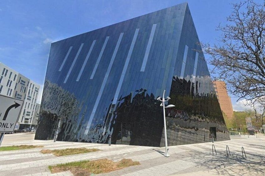 A modern building with a reflective facade and a parking lot in the foreground. 3