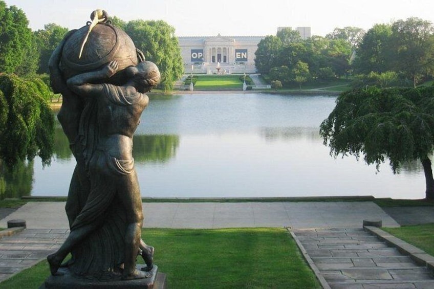 A statue of a man carrying a child, a lake, and a building with 'OP' and 'EN' signs in the background. 5