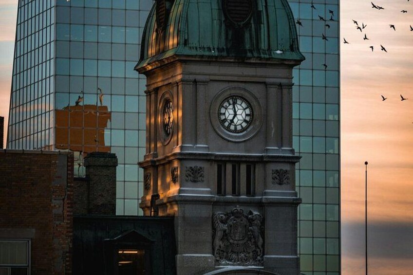 Een klokkentoren met een koepel, omgeven door moderne gebouwen en een zonsondergang. 5