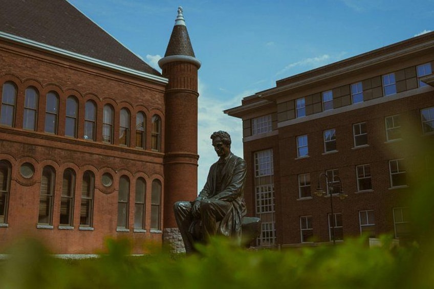 A statue in front of a red brick building with arched windows and a tower. 4