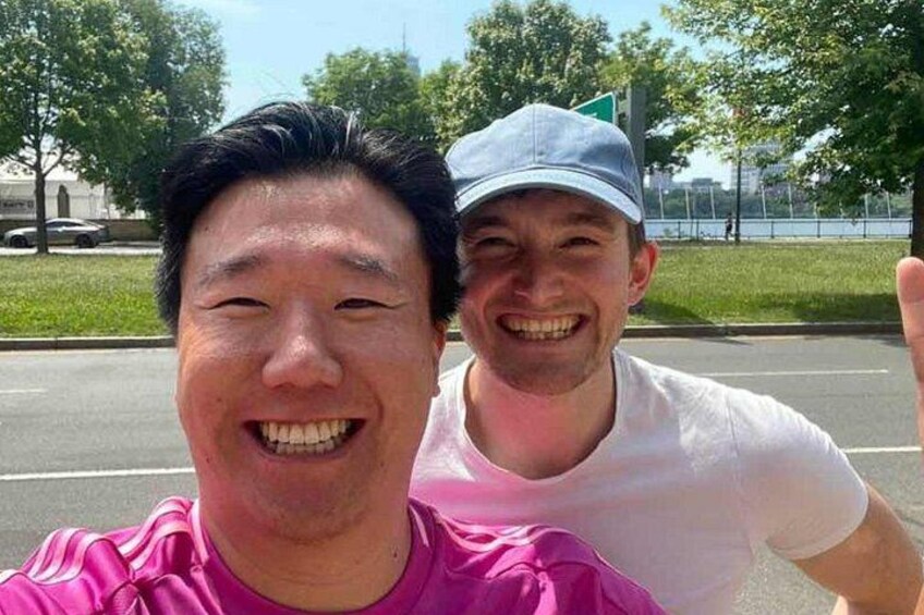 Dos personas tomándose un selfie en un estacionamiento con árboles y una carretera de fondo. 3