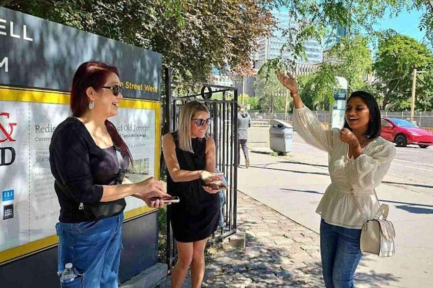 Tres mujeres de pie cerca de una parada de autobús con un cartel. 3
