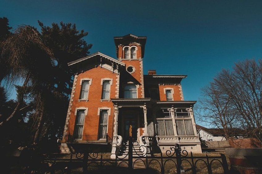 A large brick building with a tower, surrounded by trees and a wrought iron fence. 3