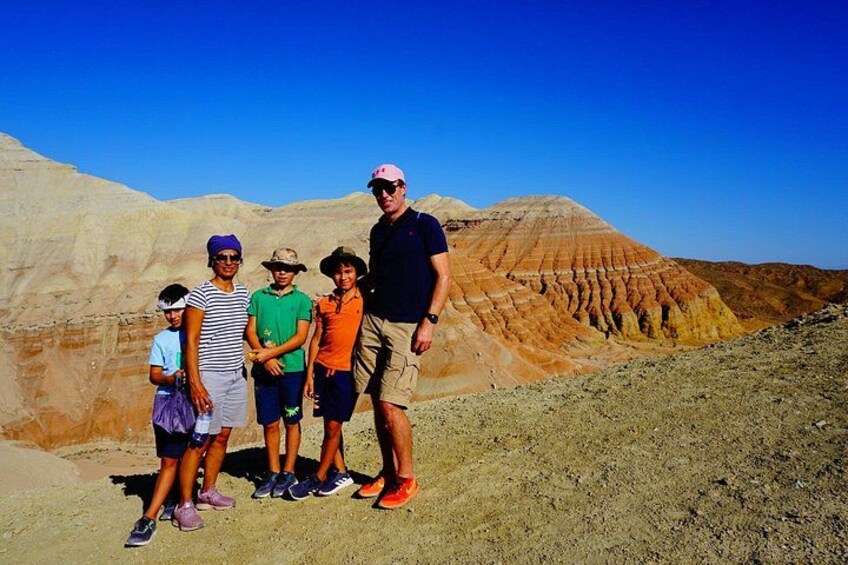 A group of people standing on a sandy terrain with layered rock formations in the background. 2