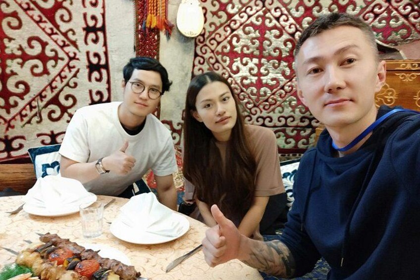 Three people sitting at a table with a meal, in a room with patterned wallpaper. 3