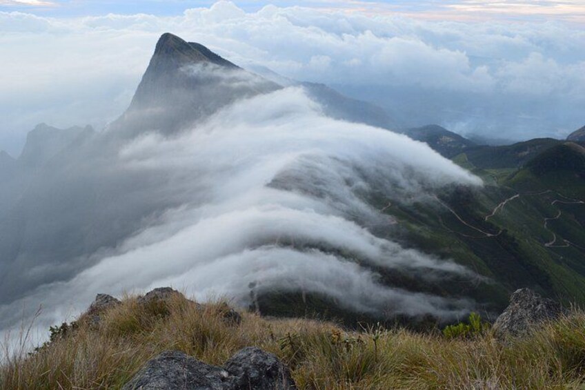 A mountain peak shrouded in clouds, with a valley below and a clear sky above. 1