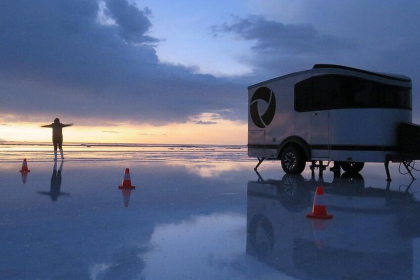 A person standing on a reflective surface with a trailer and traffic cones. 1