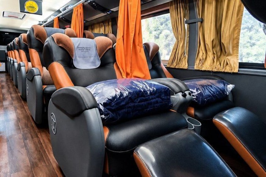 Interior de un tren con asientos de cuero, cortinas naranjas y una ventana que da a un paisaje de árboles. 1