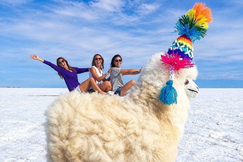 Una llama con un sombrero colorido, tres personas sentadas en su lomo, y un extenso paisaje nevado. 2