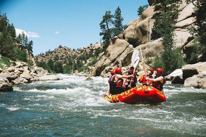 Un grupo de personas haciendo rafting por un río rodeado de terreno rocoso y árboles. 1