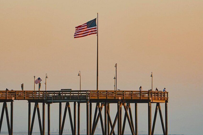 A pier with an American flag, a city skyline in the background, and a sunset sky. 3