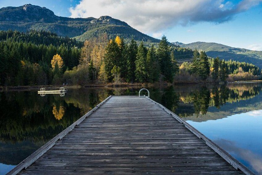 Eine Holzstege, der sich in ruhiges Wasser erstreckt, umgeben von bewaldeten Bergen und klarem Himmel. 3