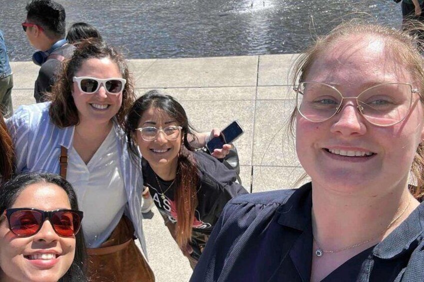 Un grupo de personas de pie junto a una costa, con un paseo de baldosas y una masa de agua al fondo. 3
