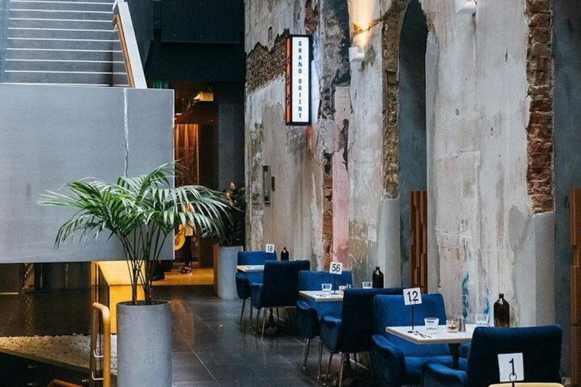 Un comedor interior con mesas y sillas azules, una planta en maceta y una pared de ladrillo con un letrero. 5