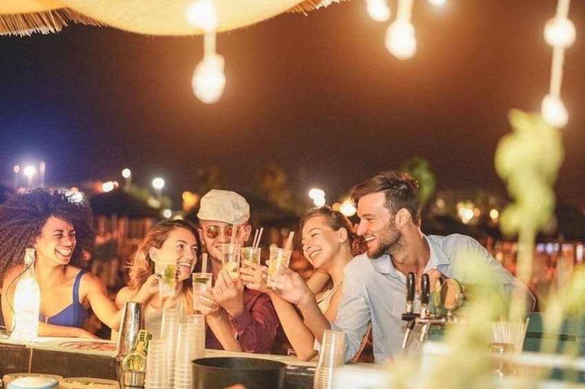 Un grupo de personas brindando con bebidas en un evento al aire libre con luces colgantes. 1