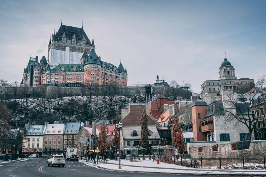 A historic building with a steep roof and multiple towers, surrounded by modern buildings and a snow-covered street. 3