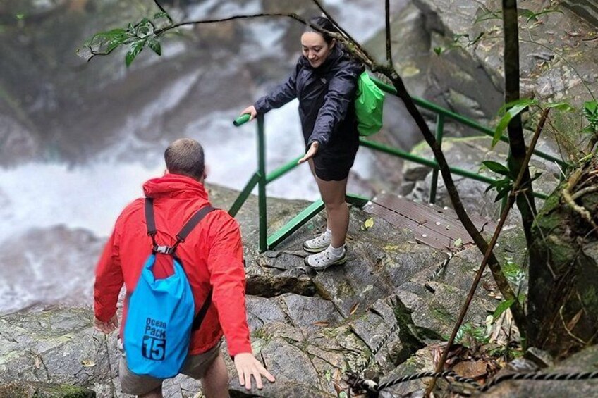 Two people hiking on a rocky path with a waterfall in the background. 4