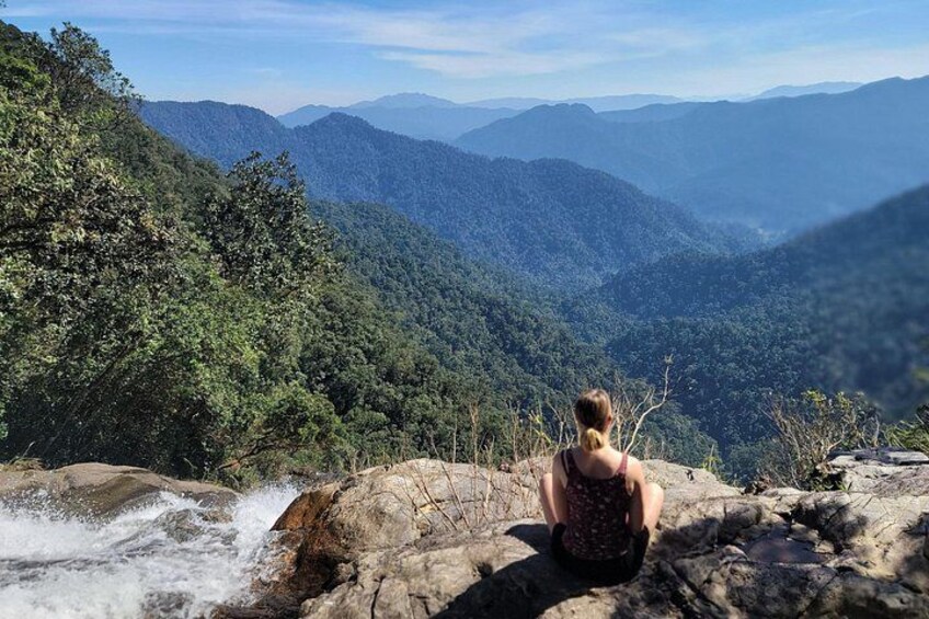 A person sitting on a rock overlooking a mountainous landscape with a waterfall. 3