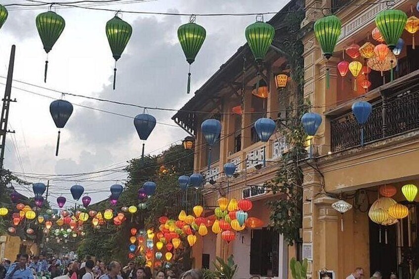 A street decorated with colorful lanterns, buildings with balconies, and a crowd of people. 2