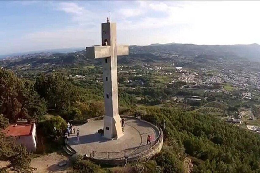 Un grande monumento a forma di croce circondato da un recinto a forma di cerchio, con vista su una città e delle colline sullo sfondo. 1