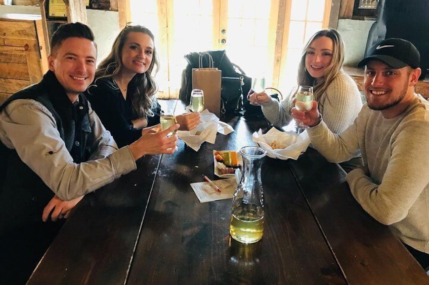 Four people sitting at a wooden table with drinks, a bottle, and a menu. 4