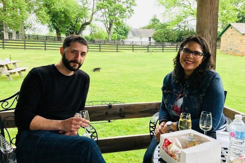 Two people sitting at a table with wine glasses, a bottle, and a box of cake. 3