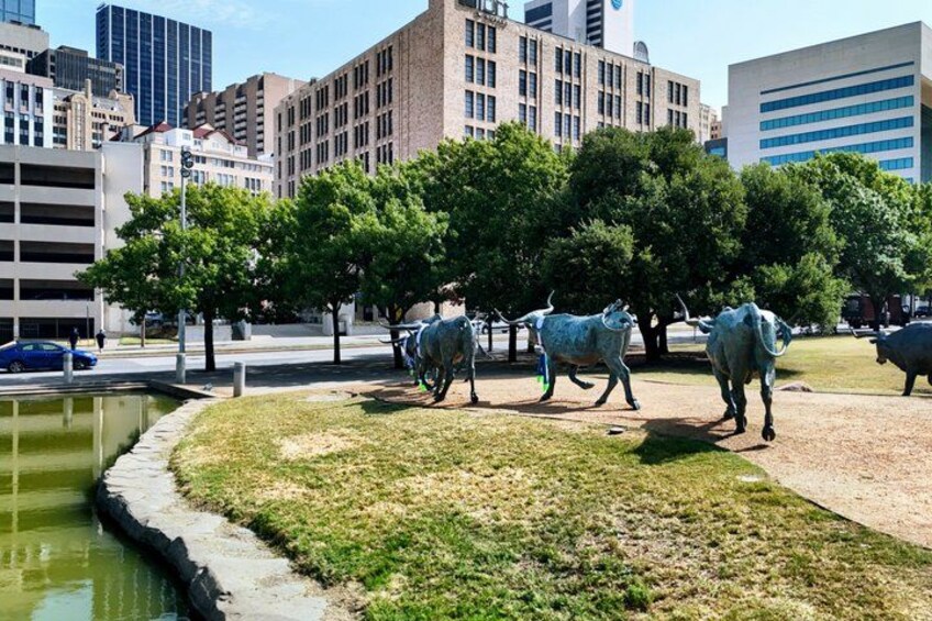 Una escultura de vacas en un parque urbano, con edificios al fondo. 3