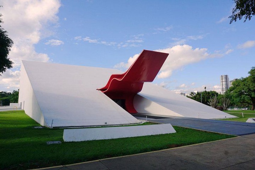 Una struttura architettonica moderna con un design bianco e rosso, immersa in un'area erbosa sotto un cielo sereno. 2
