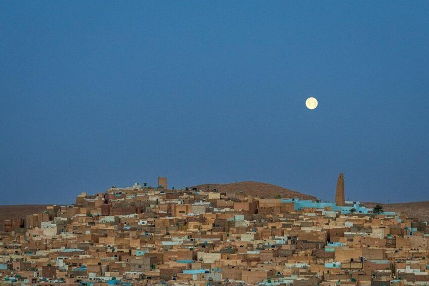 A cityscape at night with a prominent hill, a tower, and a full moon in the sky. 2