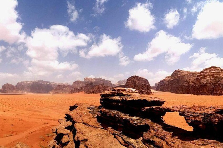 A desert landscape with rocky formations and distant mountains under a partly cloudy sky. 1