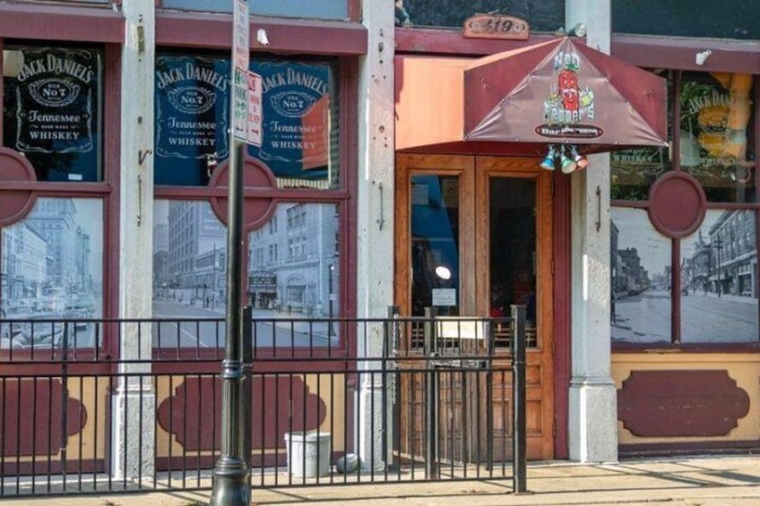 Un escaparate con toldo rojo, un cartel que dice 'Jack Daniels No. 7' y un amplio ventanal que muestra una escena callejera. 2
