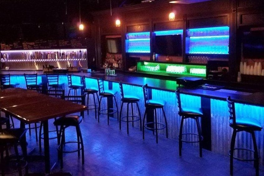 Un bar avec un comptoir et des tabourets illuminés par des néons. 2