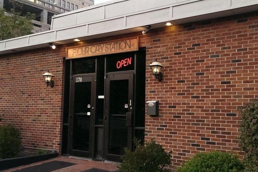 A brick building with a sign reading 'FLOUR CITY STATION OPEN' and two doors. 2