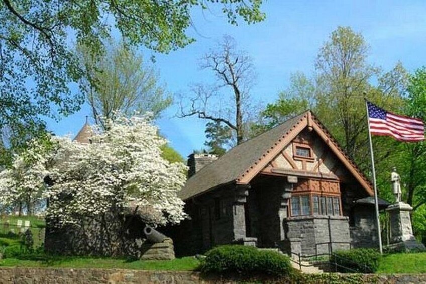 A stone cabin with a red roof, surrounded by lush greenery and a large white flowering tree. 5