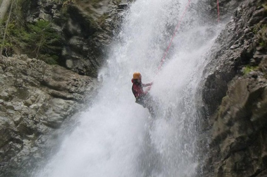 A person in a red jacket and yellow helmet descending a waterfall. 4