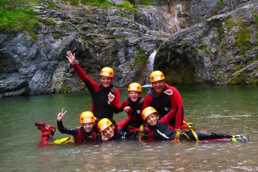 A group of people wearing helmets and life jackets, posing in a river surrounded by rocky cliffs. 5