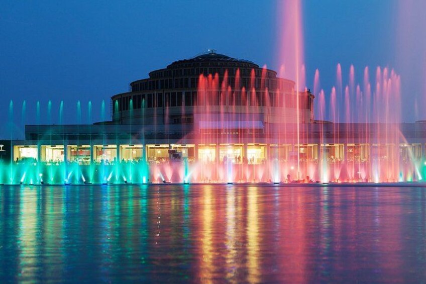 A building with a circular central section and multiple fountains in the foreground. 2