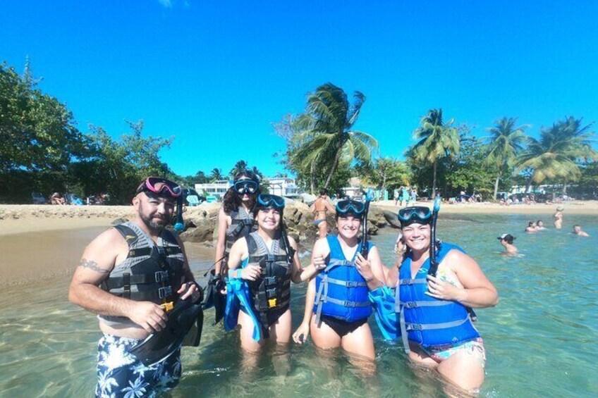 A group of people snorkeling in shallow water at a beach with palm trees and a clear blue sky in the background. 1