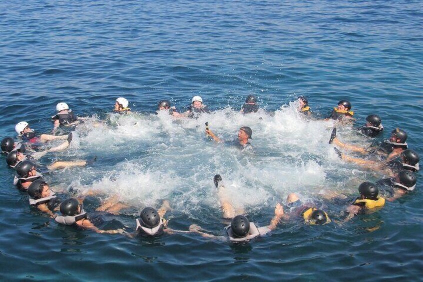 Un groupe de personnes dans l’eau, formant un cercle, portant des casques et des gilets de sauvetage. 2